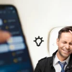 Homem confuso com app de automação residencial aberto no celular, representando erros comuns na instalação de smart home.