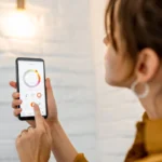 Mulher usando aplicativo de automação residencial no celular para controlar luzes