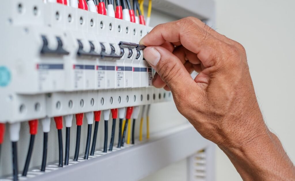 Mão de uma pessoa desligando um disjuntor no quadro elétrico residencial.
